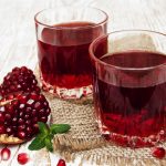 Two glasses of pomegranate juice with fresh fruits on wooden table